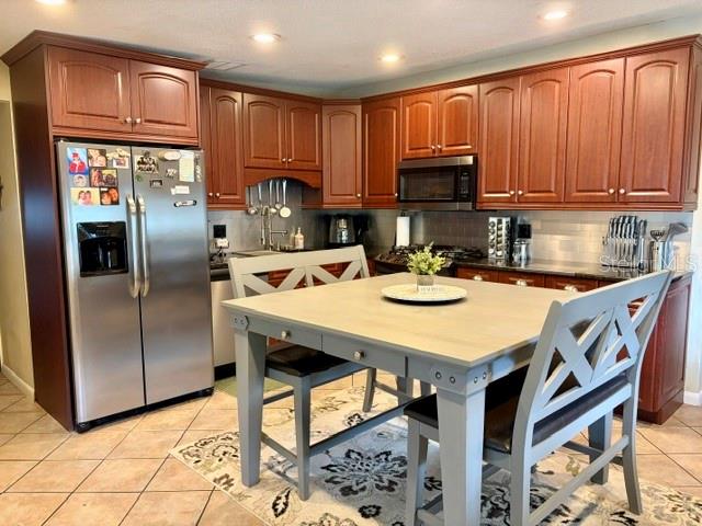 A kitchen features wood cabinets, stainless steel appliances, and a light-colored dining table with chairs — 915 HARBOR HILL DRIVE, SAFETY HARBOR, FL