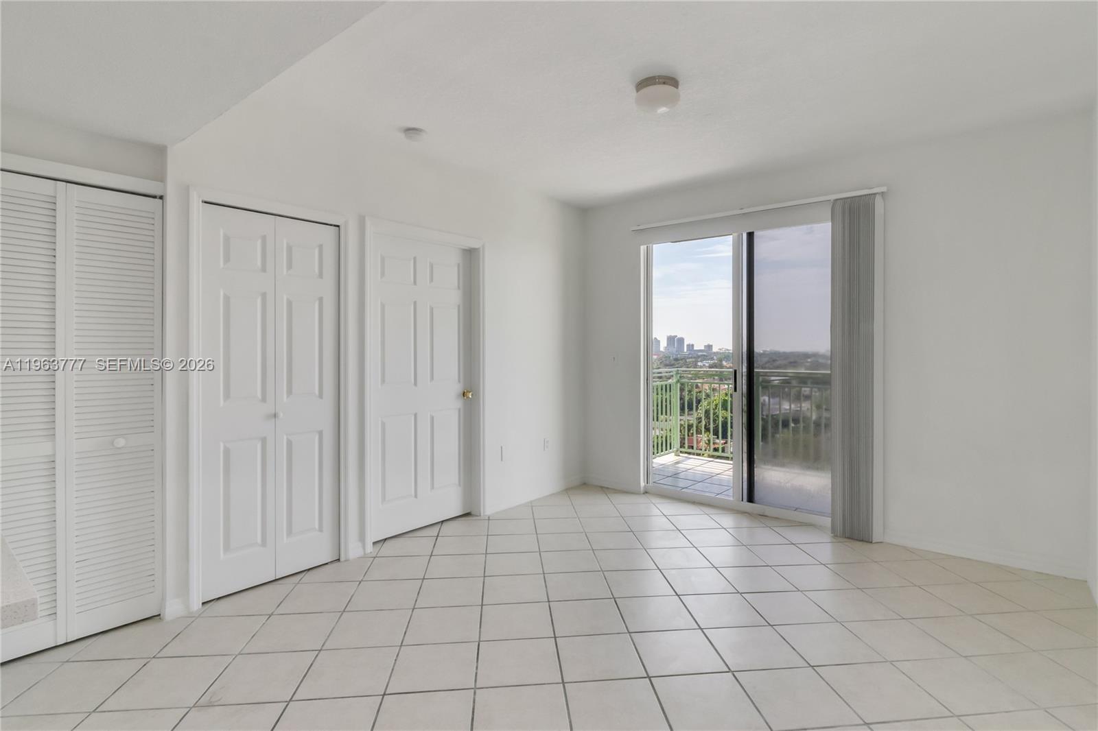 An empty room features white walls, tiled floors, closet doors, and a sliding glass balcony door — 3500 Coral Way # 1207, Miami FL 33145, MIAMI, FL