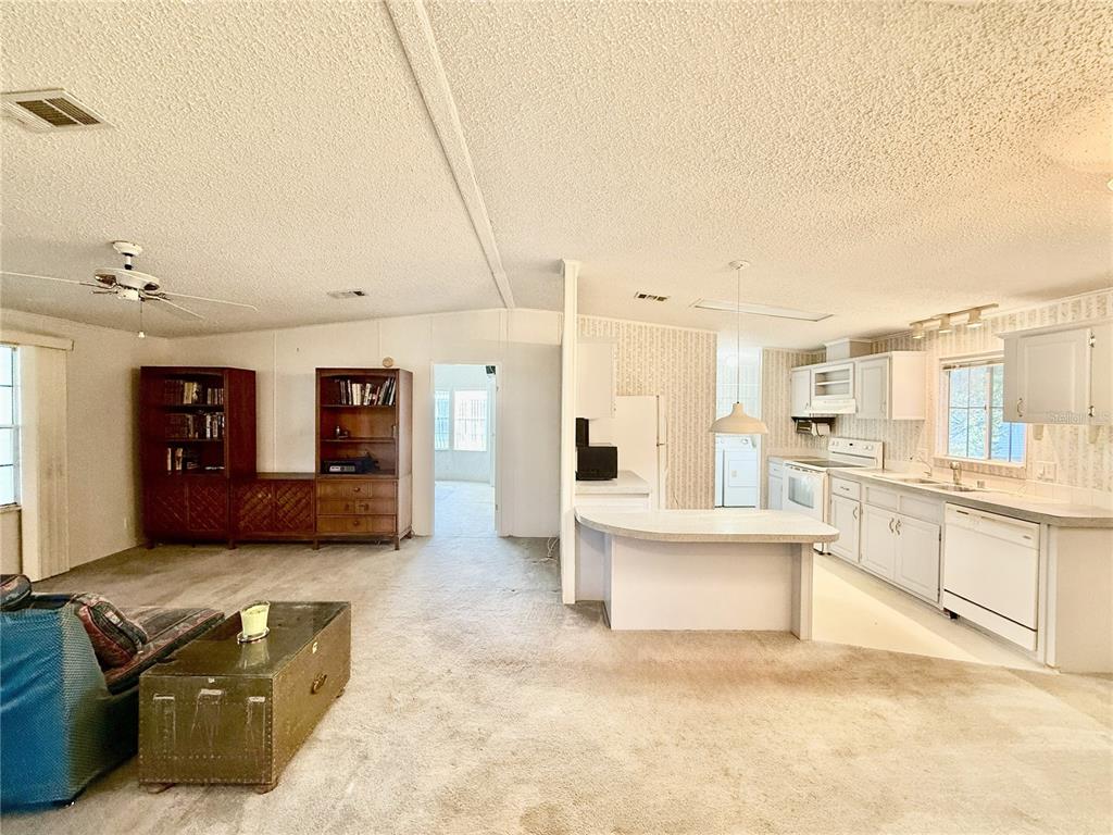 An open-concept living room and kitchen featuring beige carpeting, white cabinetry, and a breakfast bar — 5152 FOREST GLENN DRIVE, SPRING HILL, FL