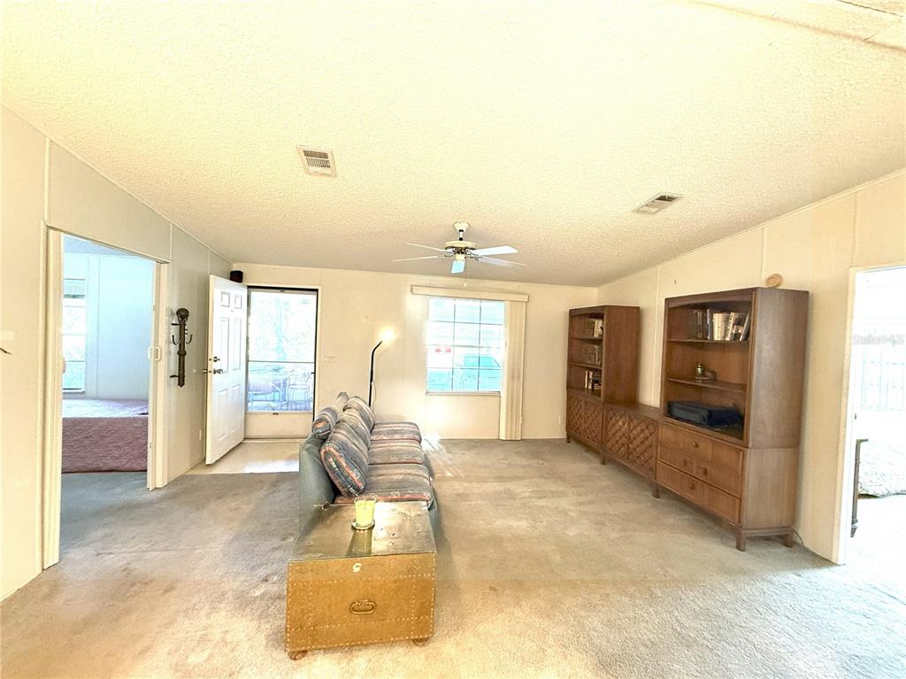 A living room features carpeted floors, a ceiling fan, and two wooden shelving units — 5152 FOREST GLENN DRIVE, SPRING HILL, FL