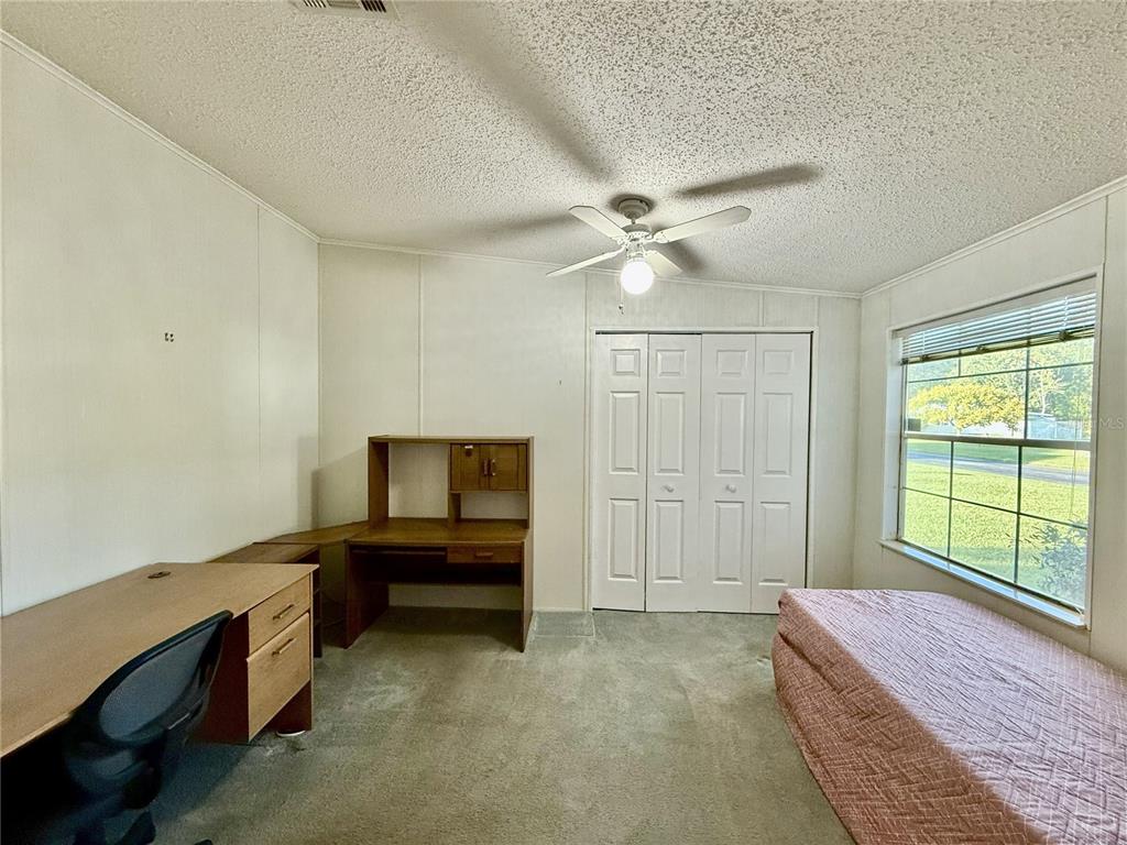 A bedroom features a low bed with a floral headboard, carpeted flooring, and three windows — 5152 FOREST GLENN DRIVE, SPRING HILL, FL