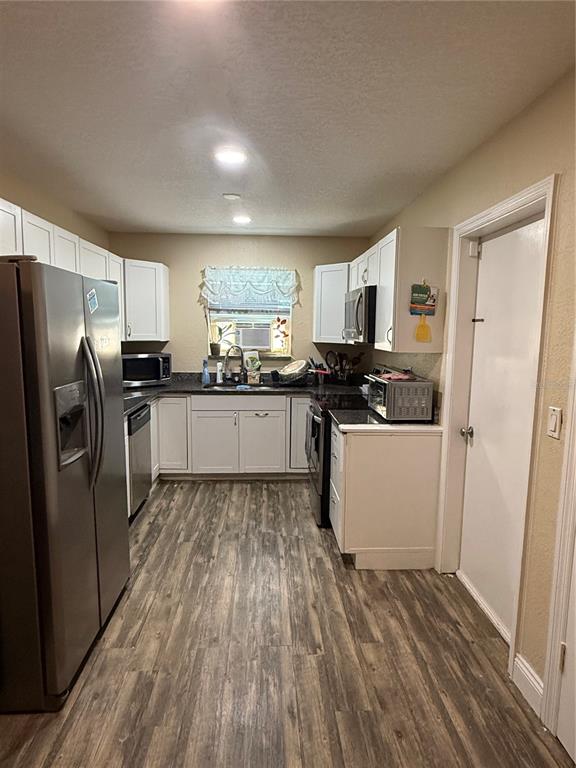 A kitchen features white cabinets, stainless steel appliances, and wood-look flooring — 1405 JACKSON AVENUE, DAYTONA BEACH, FL