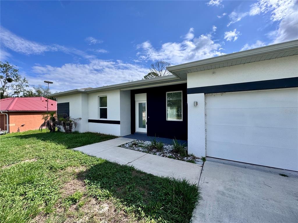 A single-story house features a white exterior with a black accent wall and garage door — 1389 WORTHINGTON DRIVE, DELTONA, FL