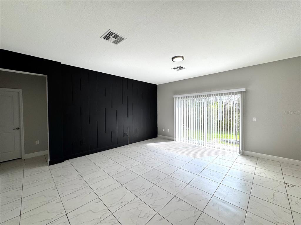 A room with white marble-look tile flooring, a black accent wall, and sliding glass doors — 1389 WORTHINGTON DRIVE, DELTONA, FL