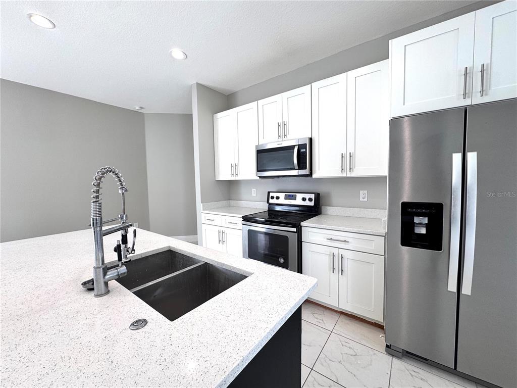 A modern kitchen features white cabinets, stainless steel appliances, and a large quartz-topped island — 1389 WORTHINGTON DRIVE, DELTONA, FL