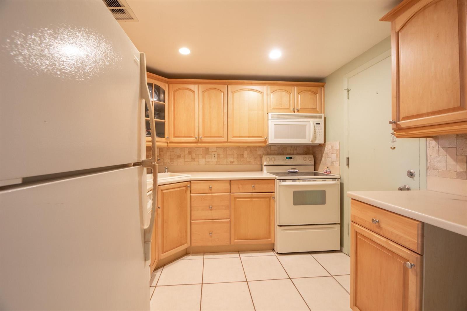 A kitchen features light wood cabinets, white appliances, a tiled backsplash, and white floor tiles — 305 N Pompano Beach Boulevard # 505, Pompano Beach FL 33062, POMPANO BEACH, FL