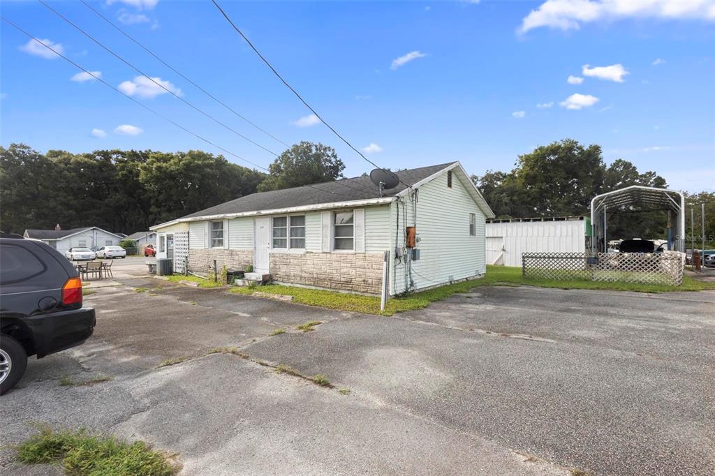 A light-colored house with stone accents and a large paved parking area — 2490 N WOODLAND BOULEVARD, DELAND, FL
