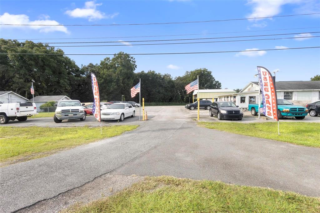 A car dealership lot features several parked vehicles, American flags, and promotional banners — 2490 N WOODLAND BOULEVARD, DELAND, FL