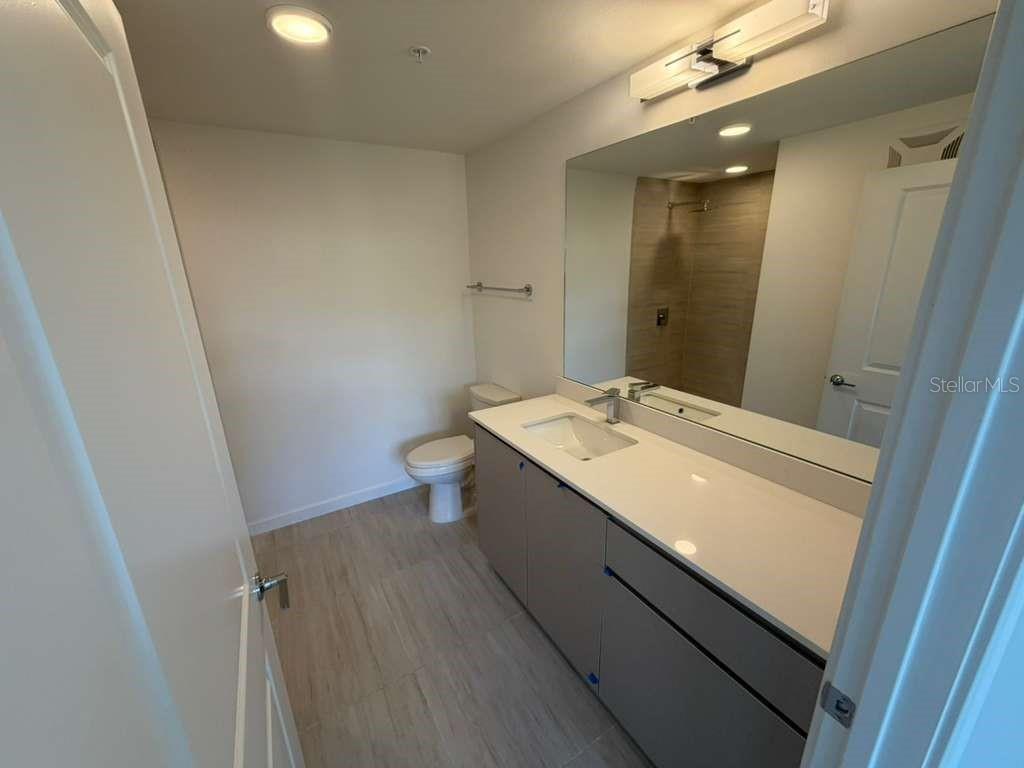 A modern bathroom features a gray vanity with a white countertop, toilet, and large mirror — 5587 MILLENIA PARK BOULEVARD UNIT 202, ORLANDO, FL