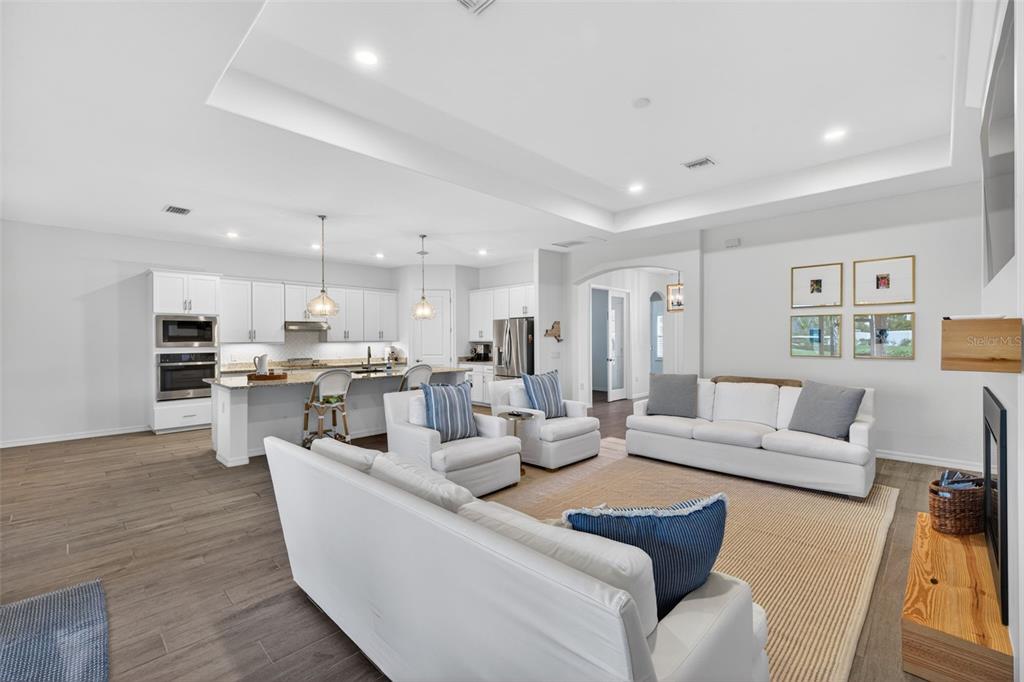 An open-concept living room and kitchen featuring white cabinetry, light wood flooring, and neutral furniture — 25000 HALLIANA LANE, PUNTA GORDA, FL