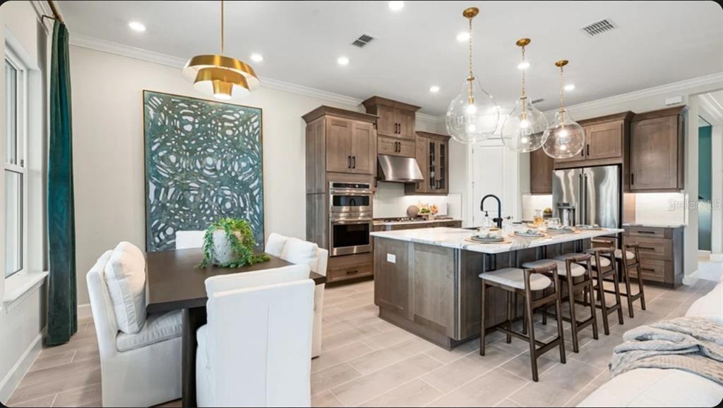 A kitchen and dining area featuring wooden cabinets, a large island, and modern pendant lighting — 7672 MOONBEAM AVENUE, SARASOTA, FL