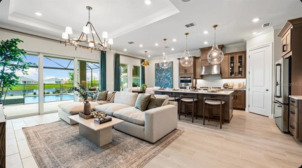 An open-concept living room and kitchen featuring light wood floors, a large island, and pool views — 7672 MOONBEAM AVENUE, SARASOTA, FL