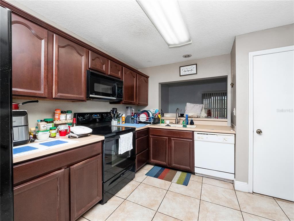A kitchen features dark wood cabinets, black appliances, a white dishwasher, and tiled flooring — 2329 WATER VIEW LOOP, KISSIMMEE, FL