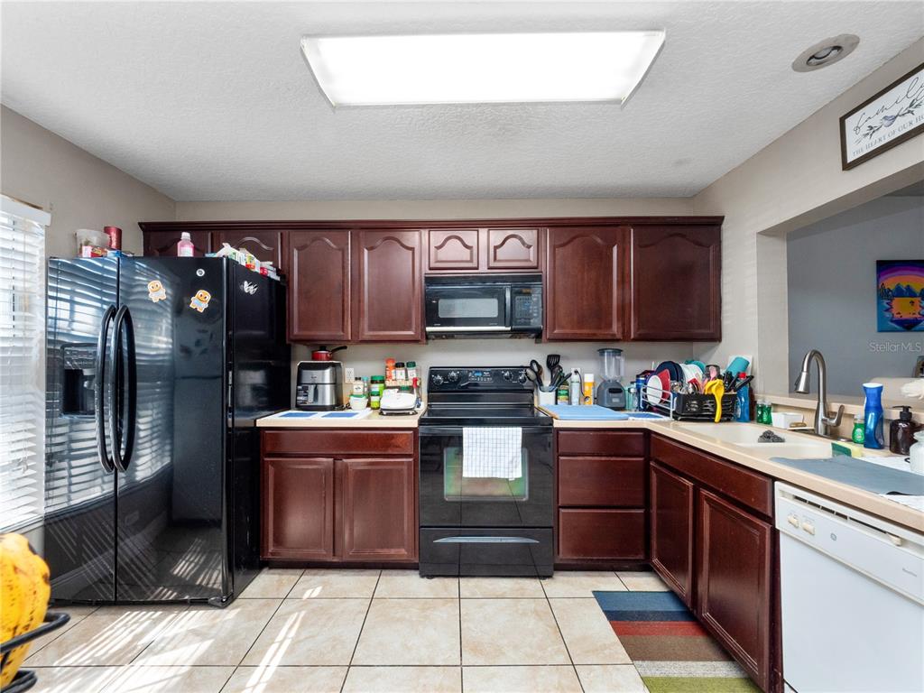A kitchen features dark wood cabinets, black appliances, and light-colored tile flooring — 2329 WATER VIEW LOOP, KISSIMMEE, FL
