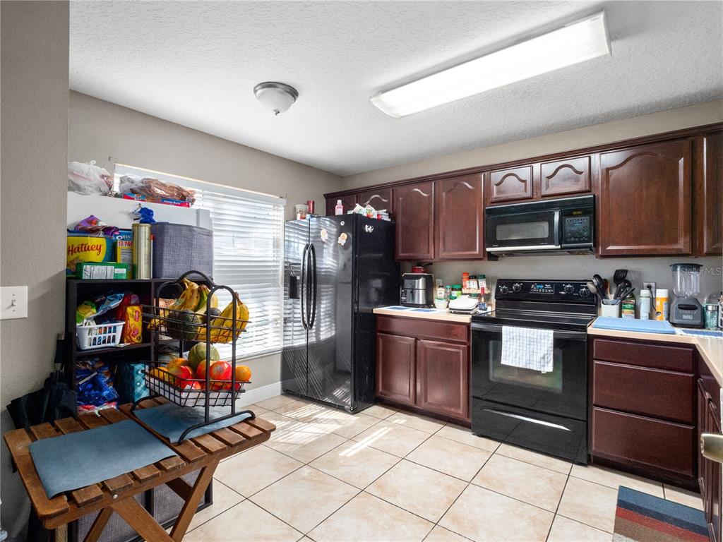 A kitchen features dark wood cabinets, black appliances, tile flooring, and a window with blinds — 2329 WATER VIEW LOOP, KISSIMMEE, FL