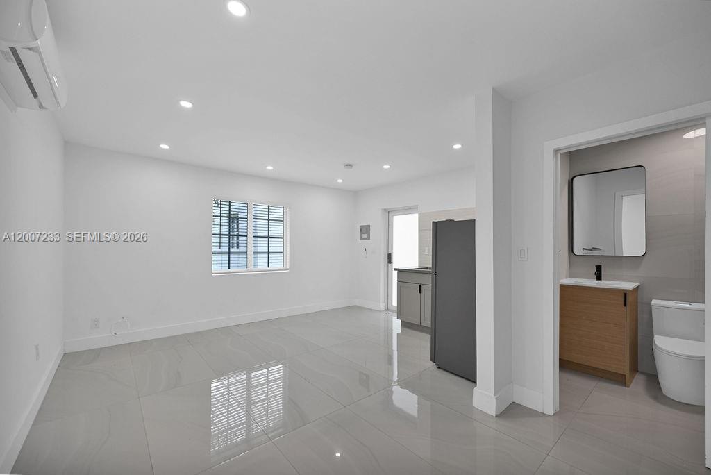 A bright, minimalist room features white walls, light tile flooring, a small kitchenette, and a bathroom — 570 NW 48th St # B, Miami FL 33127, MIAMI, FL