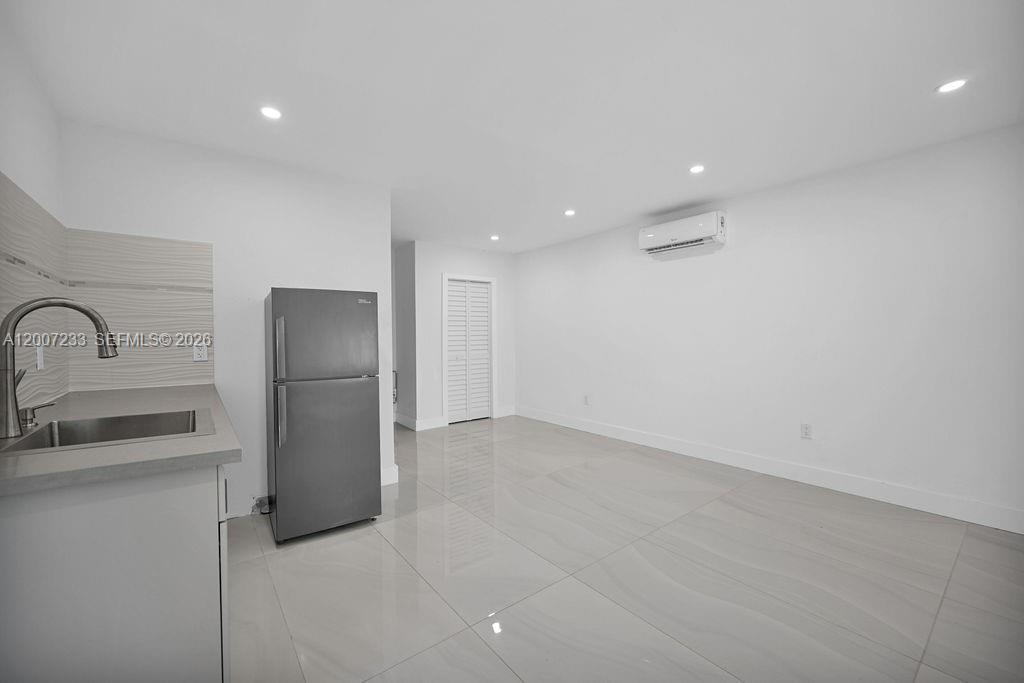 A modern kitchen and living area features white walls, tile flooring, and a stainless refrigerator — 570 NW 48th St # B, Miami FL 33127, MIAMI, FL