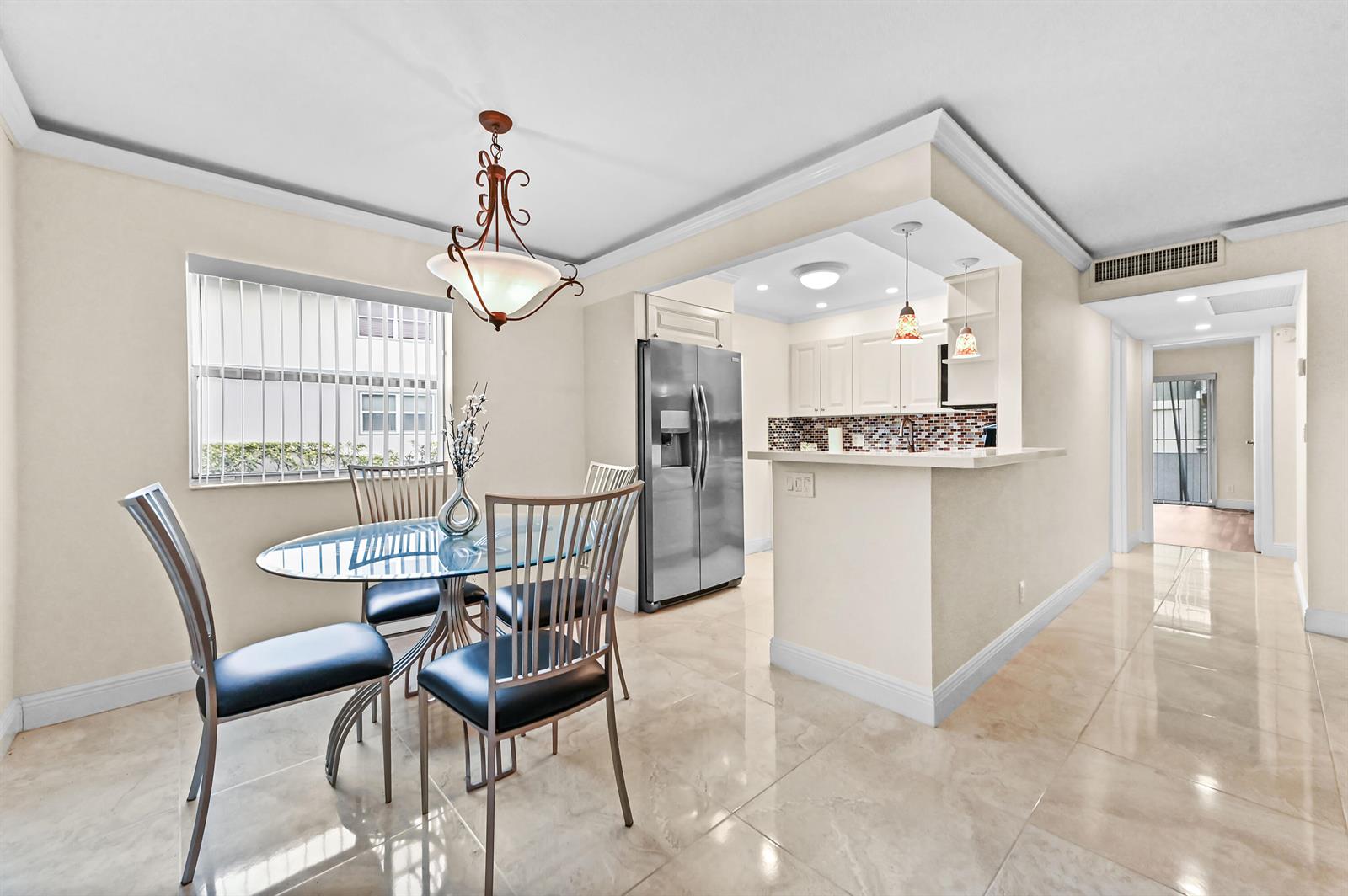 A dining area with a glass table and chairs sits adjacent to an open kitchen — 205 Flanders E, Delray Beach FL 33484, DELRAY BEACH, FL