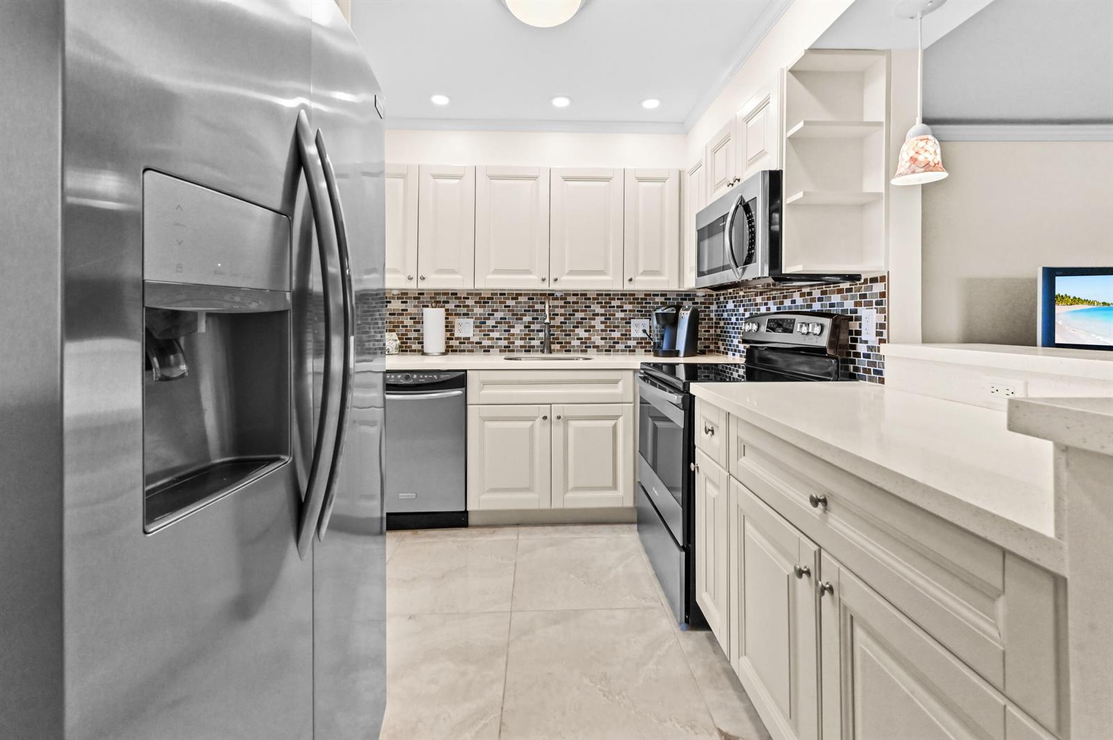 A kitchen features white cabinets, stainless steel appliances, a mosaic tile backsplash, and light countertops — 205 Flanders E, Delray Beach FL 33484, DELRAY BEACH, FL