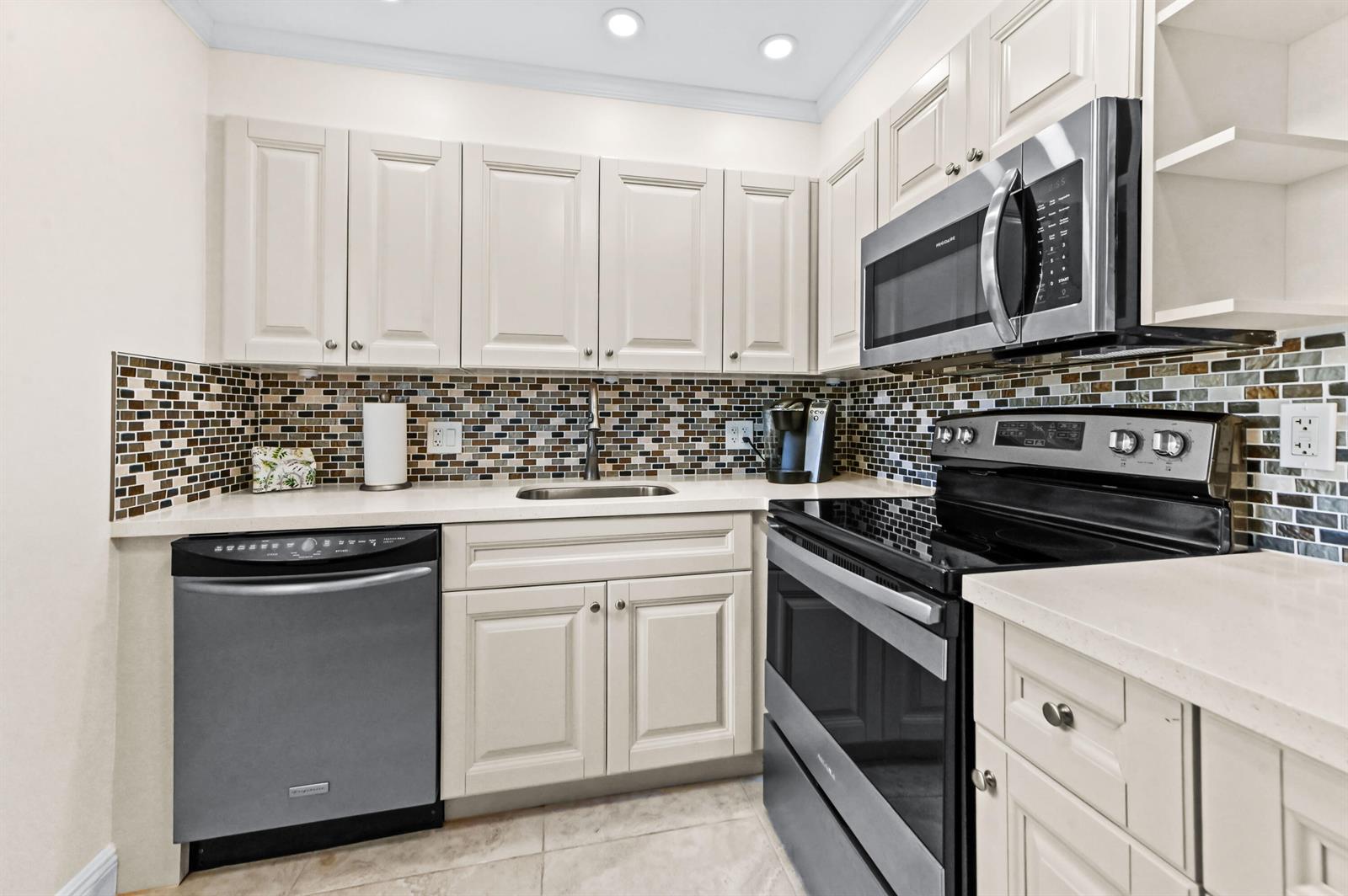 A kitchen features off-white cabinets, stainless steel appliances, a mosaic tile backsplash, and light countertops — 205 Flanders E, Delray Beach FL 33484, DELRAY BEACH, FL