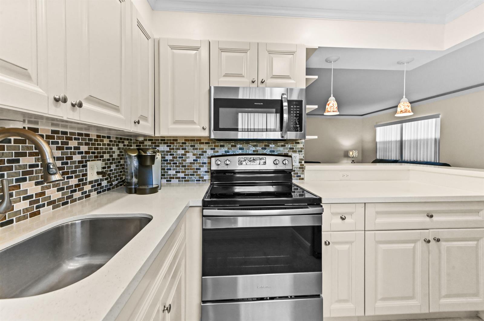 A kitchen features white cabinetry, stainless steel appliances, a mosaic tile backsplash, and quartz countertops — 205 Flanders E, Delray Beach FL 33484, DELRAY BEACH, FL