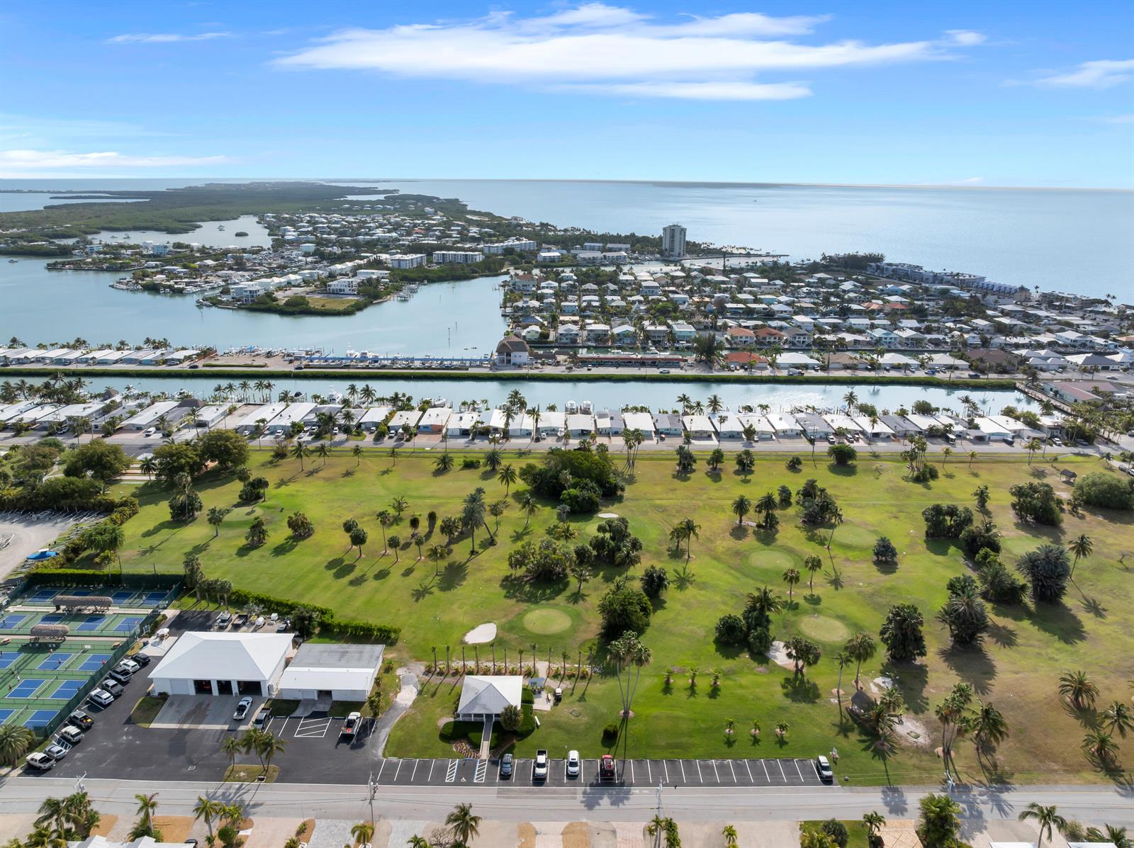 An aerial view shows a golf course, tennis courts, and a residential area near water — 34 7th Street, FL 33051, FL
