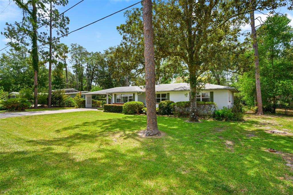 A single-story white house with a carport sits on a grassy lot with mature trees — 3919 SW 4TH PLACE, GAINESVILLE, FL