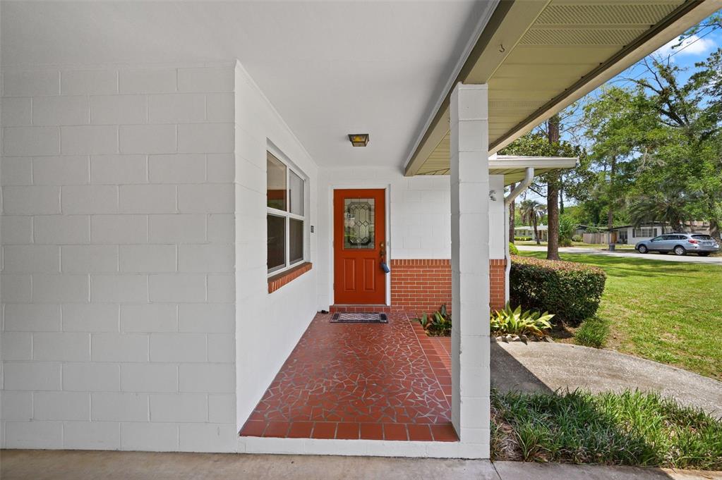 A covered porch features a red door, brick accents, and a tiled floor — 3919 SW 4TH PLACE, GAINESVILLE, FL