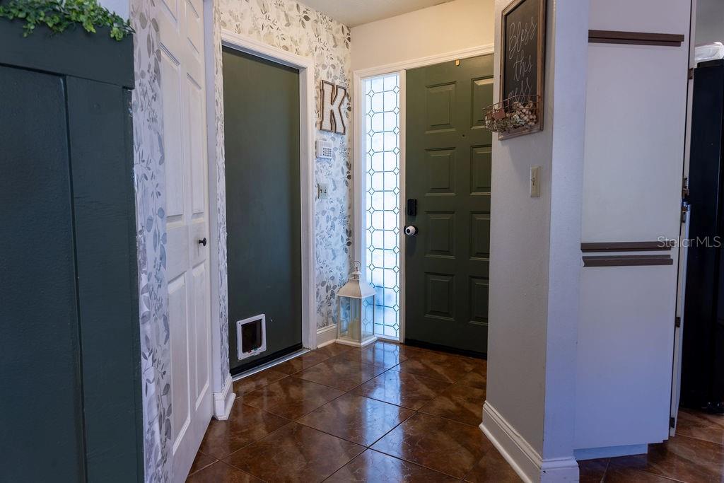 An entryway features tiled floors, a green front door with sidelights, and floral wallpaper — 1707 WHISPERING DRIVE E, LARGO, FL