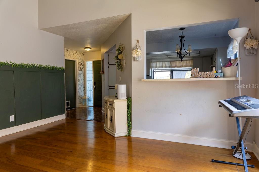 A living area with hardwood floors, a green wainscoted wall, and a kitchen pass-through window — 1707 WHISPERING DRIVE E, LARGO, FL