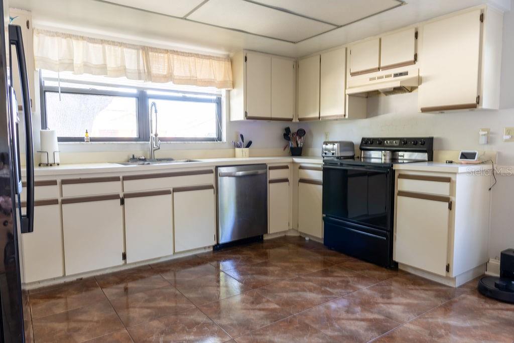A kitchen with off-white cabinets, black appliances, a stainless steel dishwasher, and brown tile flooring — 1707 WHISPERING DRIVE E, LARGO, FL