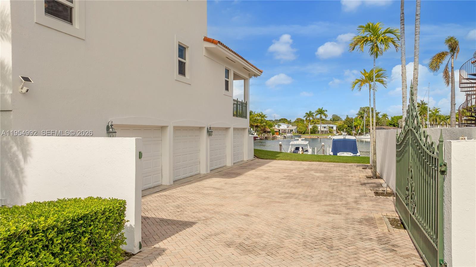 A paved driveway leads to a four-car garage beside a waterfront canal with boats — 6275 Dolphin Dr, Coral Gables FL 33158, CORAL GABLES, FL