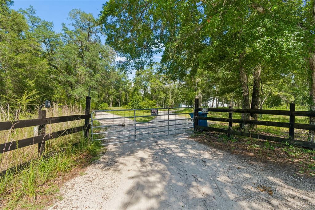 A metal gate blocks a dirt driveway between wooden fences surrounded by lush green trees — 3140 CRUM ROAD, BROOKSVILLE, FL
