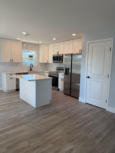 A modern kitchen features white cabinets, stainless steel appliances, a center island, and wood flooring — 521 SKYLINE DRIVE E, LAKELAND, FL