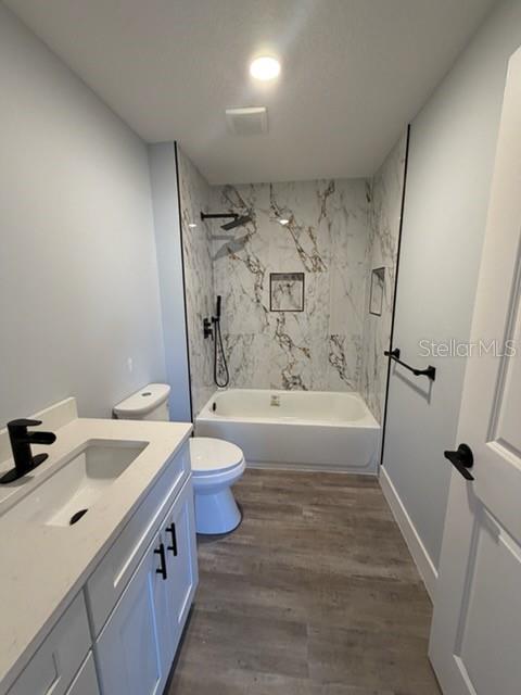 A bathroom features a white vanity, a toilet, and a bathtub with marble-patterned tile walls — 521 SKYLINE DRIVE E, LAKELAND, FL