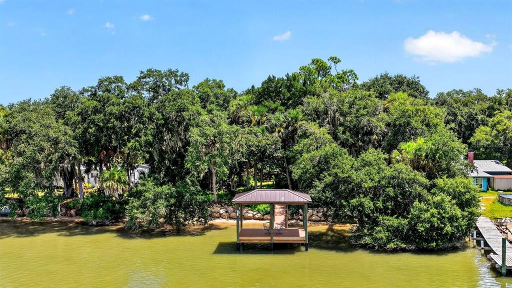 A wooden boat dock with a roof sits on a lake in front of dense trees — 114 HERNANDEZ AVENUE, PALM COAST, FL