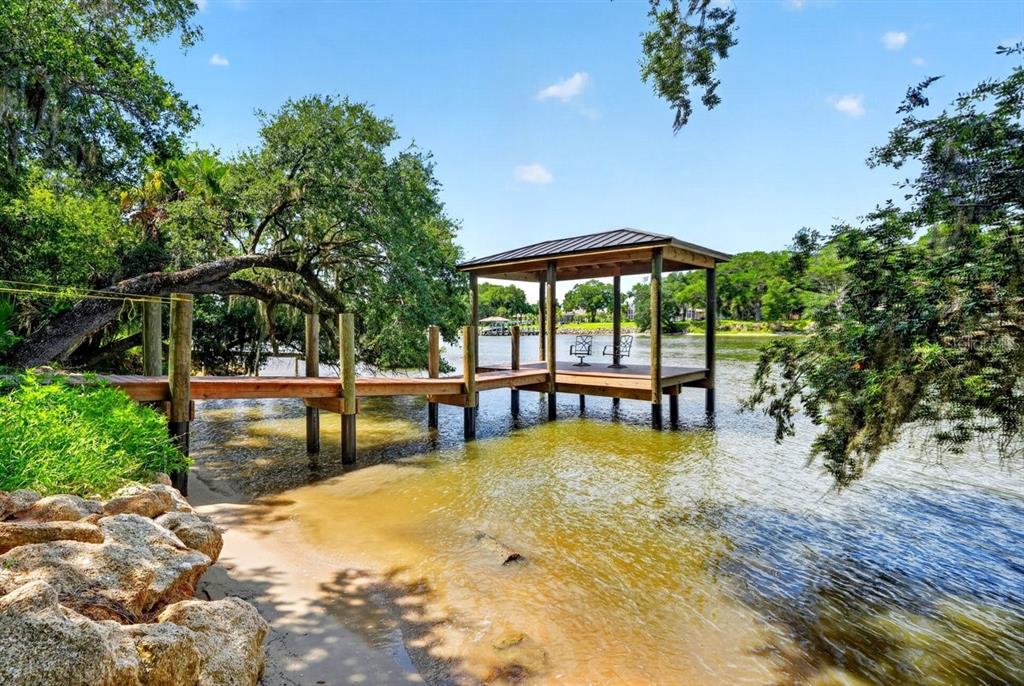A wooden dock with a covered gazebo extends over a lake near a sandy shore — 114 HERNANDEZ AVENUE, PALM COAST, FL