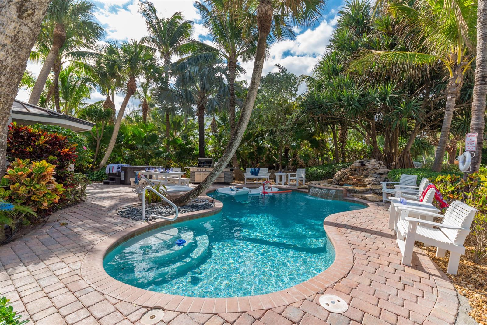 A backyard swimming pool with a rock waterfall, patio furniture, and lush tropical landscaping — 4643 NE Ocean Boulevard, Jensen Beach FL 34957, JENSEN BEACH, FL