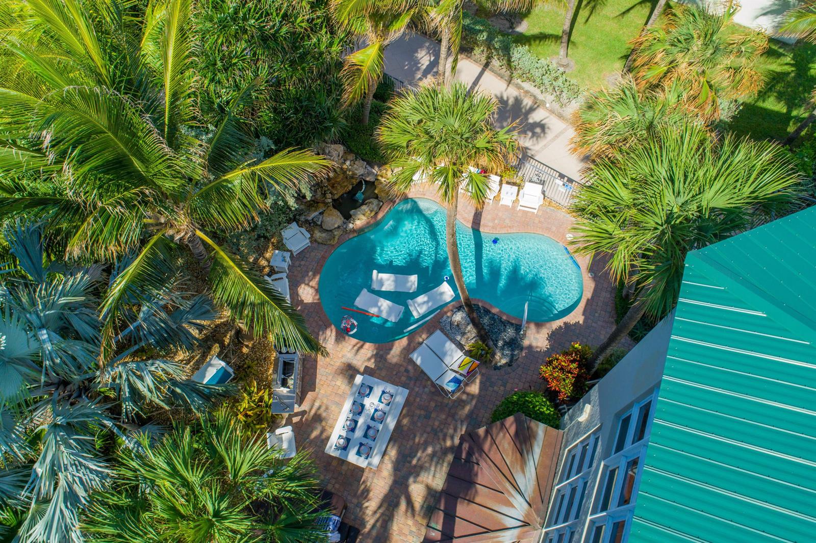 An aerial view shows a swimming pool with lounge chairs, a patio, and palm trees — 4643 NE Ocean Boulevard, Jensen Beach FL 34957, JENSEN BEACH, FL
