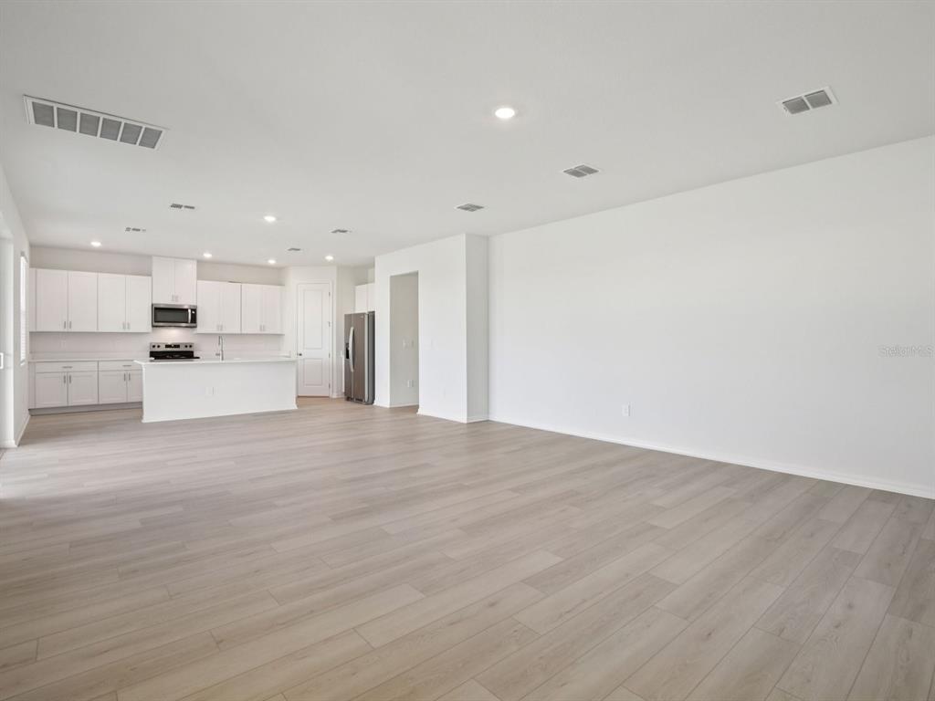 An open-concept kitchen and living area feature white cabinetry, stainless appliances, and light wood flooring — 9017 VENETIA COURT, PALMETTO, FL