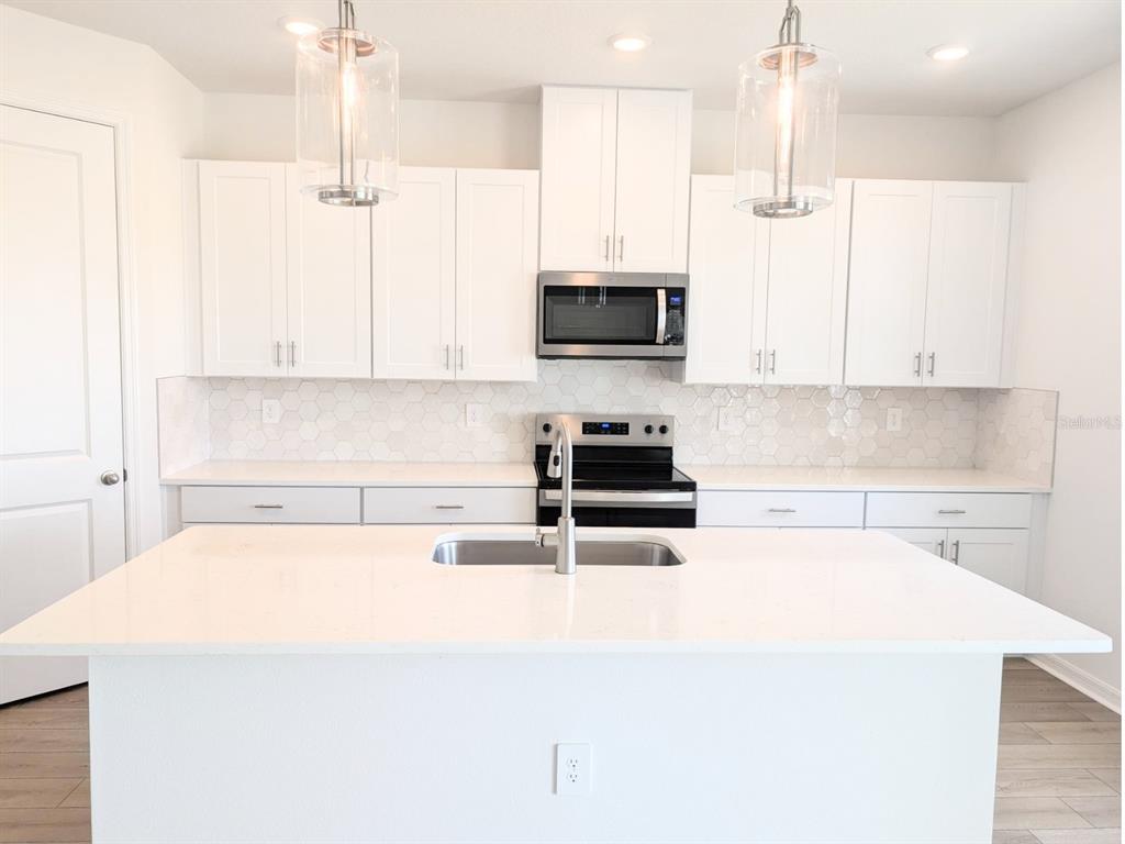 A modern kitchen features white cabinets, a central island, stainless steel appliances, and hexagon backsplash — 9017 VENETIA COURT, PALMETTO, FL