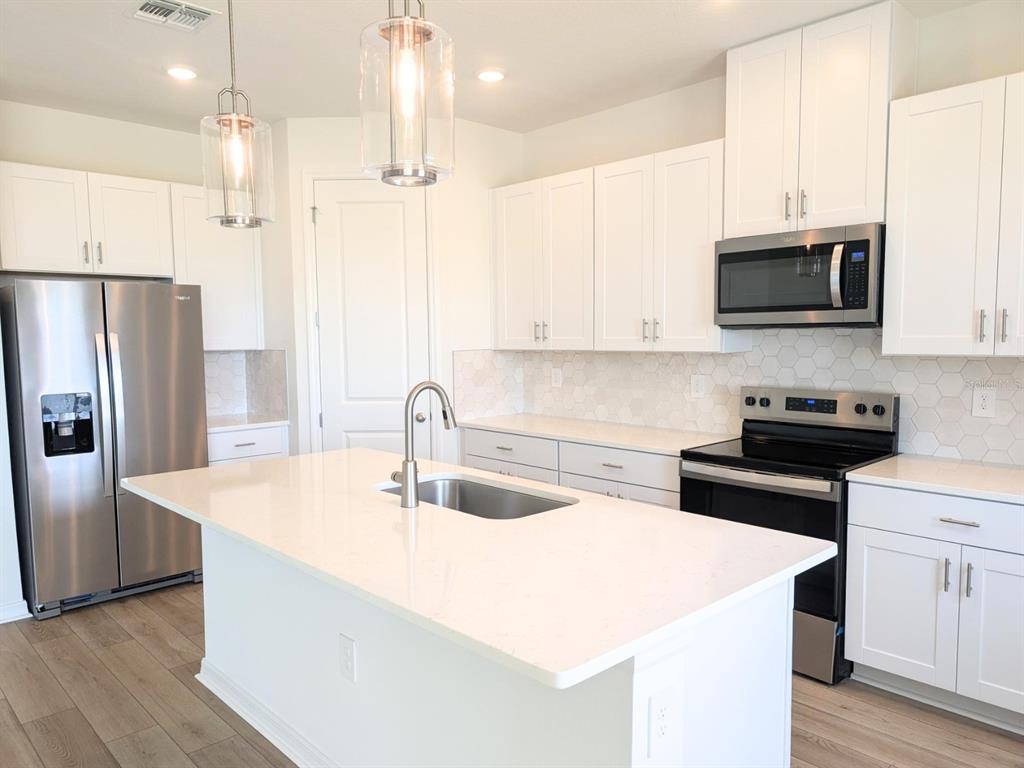 A modern kitchen features white cabinets, stainless steel appliances, a quartz island, and wood flooring — 9017 VENETIA COURT, PALMETTO, FL