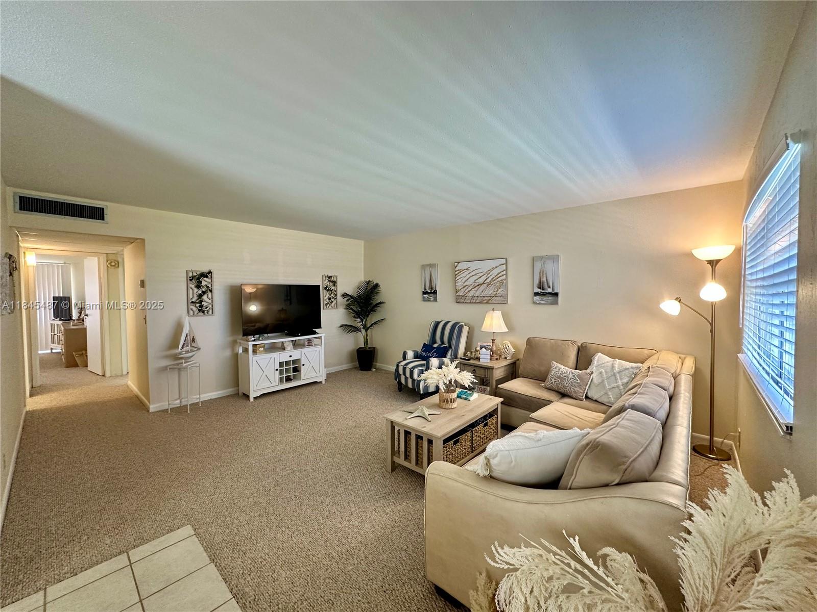A living room features a beige sectional sofa, a television on a white stand, and carpet — 524 Monaco K # 524K, Delray Beach FL 33446, DELRAY BEACH, FL
