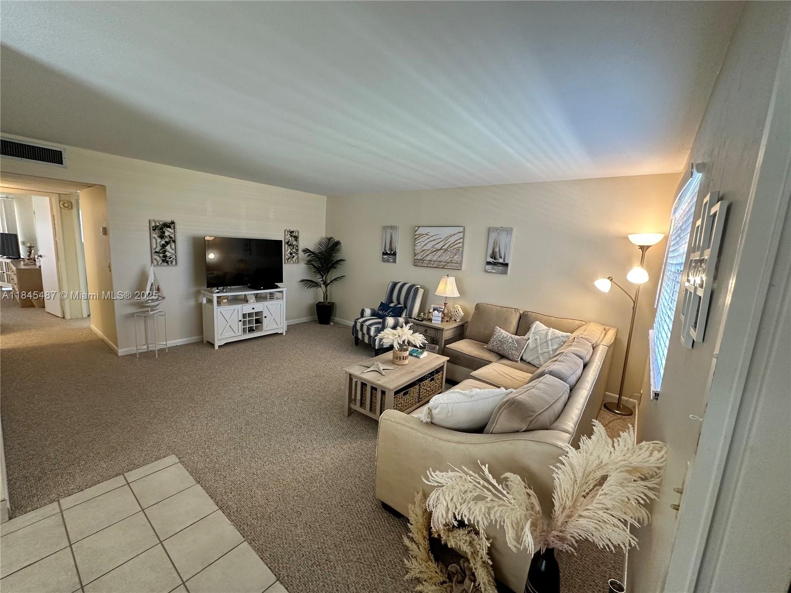 A living room features beige carpet, a sectional sofa, a television, and coastal-themed decor — 524 Monaco K # 524K, Delray Beach FL 33446, DELRAY BEACH, FL
