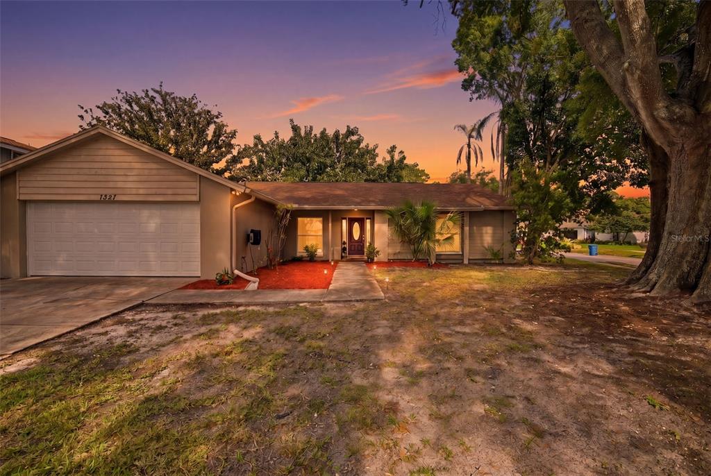 A single-story house with a garage and red mulch landscaping at sunset — 7327 SUNSHINE CIRCLE, TAMPA, FL
