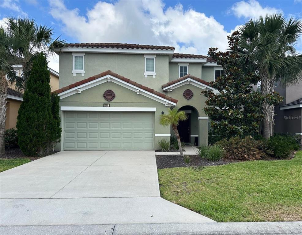 A two-story house with a green stucco exterior, a two-car garage, and a tiled roof — 5299 WILDWOOD WAY, DAVENPORT, FL