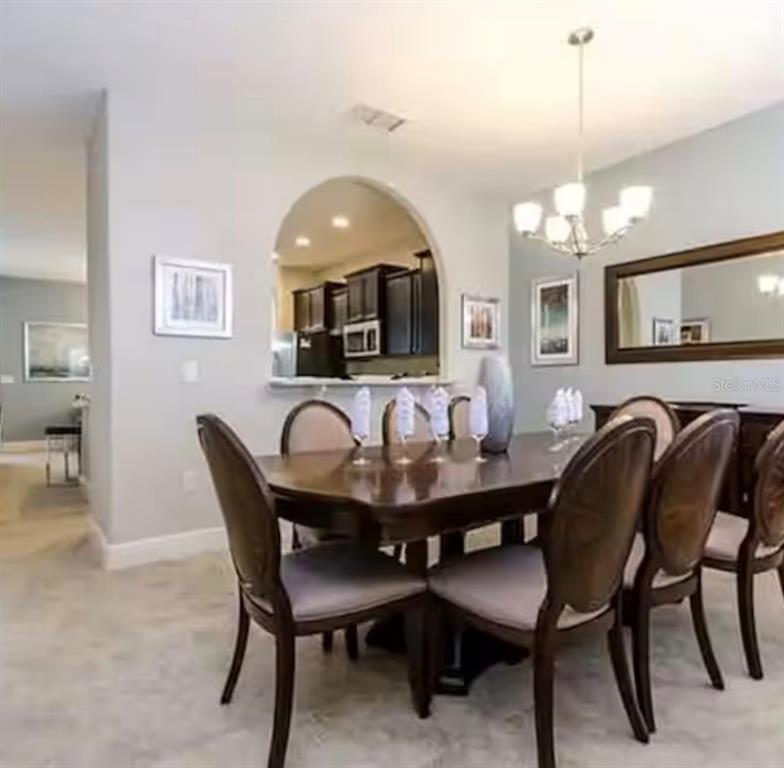 A dining room features a dark wood table, upholstered chairs, and an arched kitchen pass-through — 5299 WILDWOOD WAY, DAVENPORT, FL