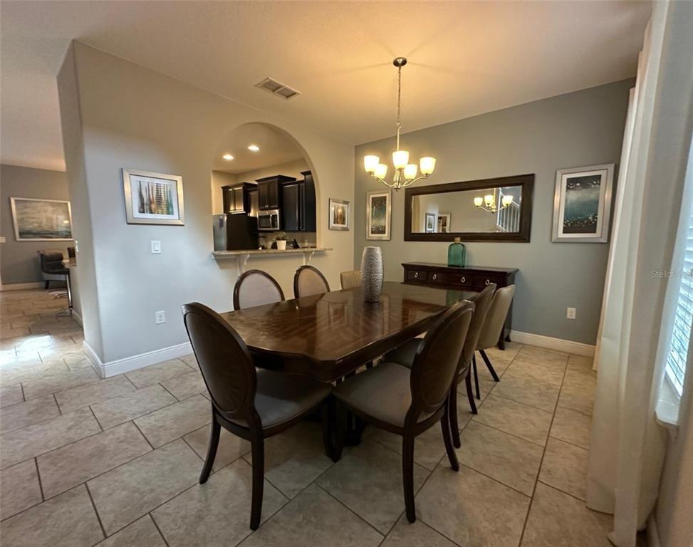 A dining room features a wooden table, upholstered chairs, a chandelier, and an arched entryway — 5299 WILDWOOD WAY, DAVENPORT, FL