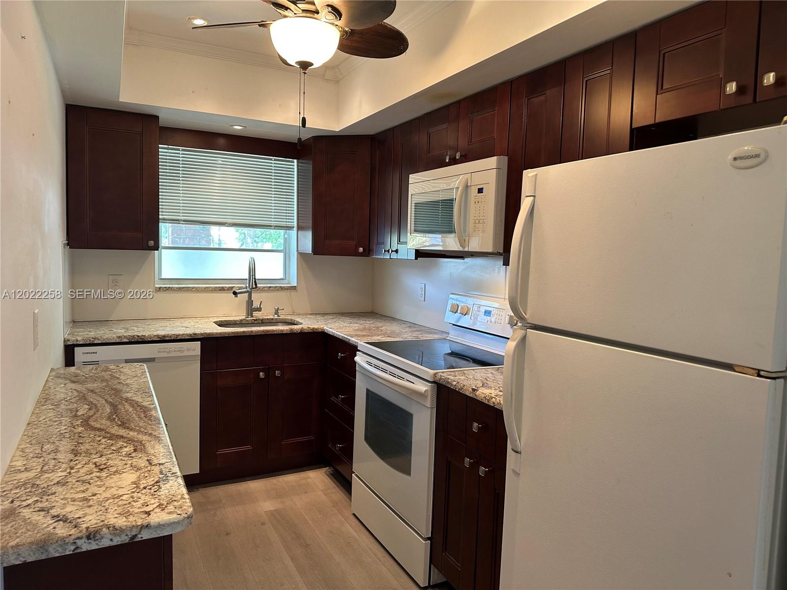 A kitchen features dark wood cabinets, granite countertops, white appliances, and light wood flooring — 3700 Harrison St # 15A, Hollywood FL 33021, HOLLYWOOD, FL