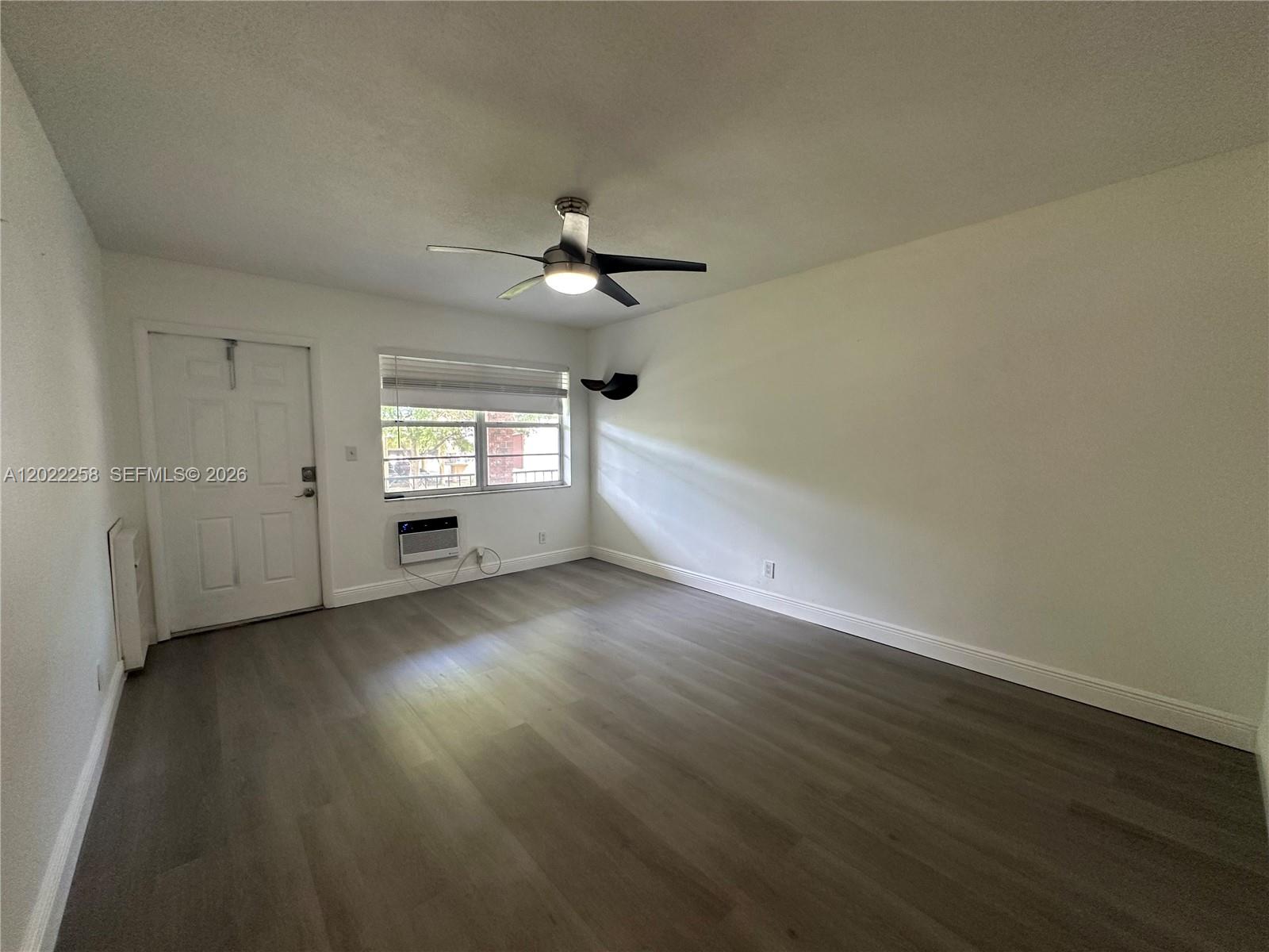 An empty room features white walls, gray wood-look flooring, a ceiling fan, and a window unit — 3700 Harrison St # 15A, Hollywood FL 33021, HOLLYWOOD, FL